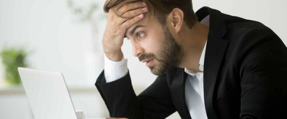 Worried stressed businessman in suit shocked by bad news using laptop