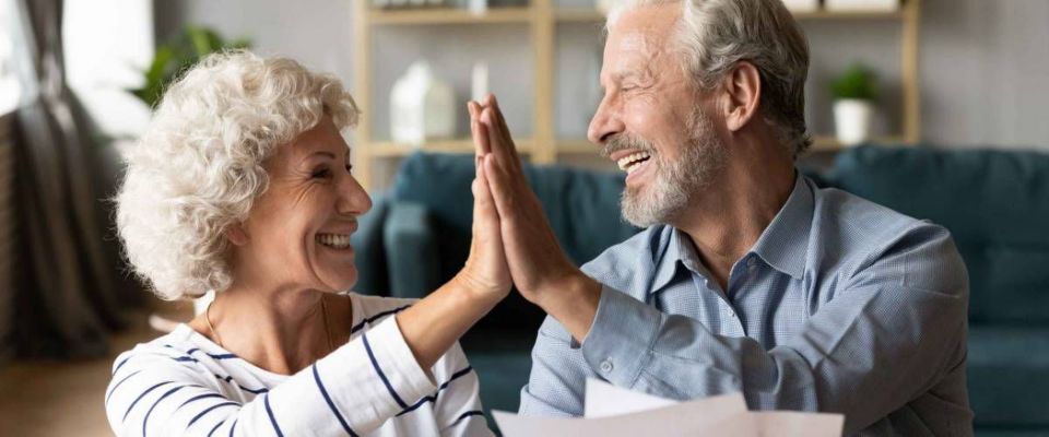 Excited older couple giving high five, mature family celebrating success, checking or paying domestic bills, planning budget, smiling mature man holding financial documents, reading good news