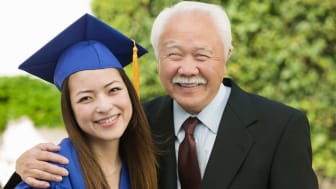 Grandfather hugging granddaughter wearing college graduation cap and gown