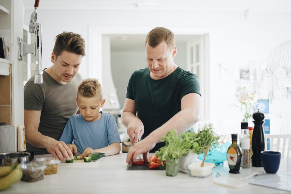 Homosexual fathers and son cutting cucumber in kitchen
