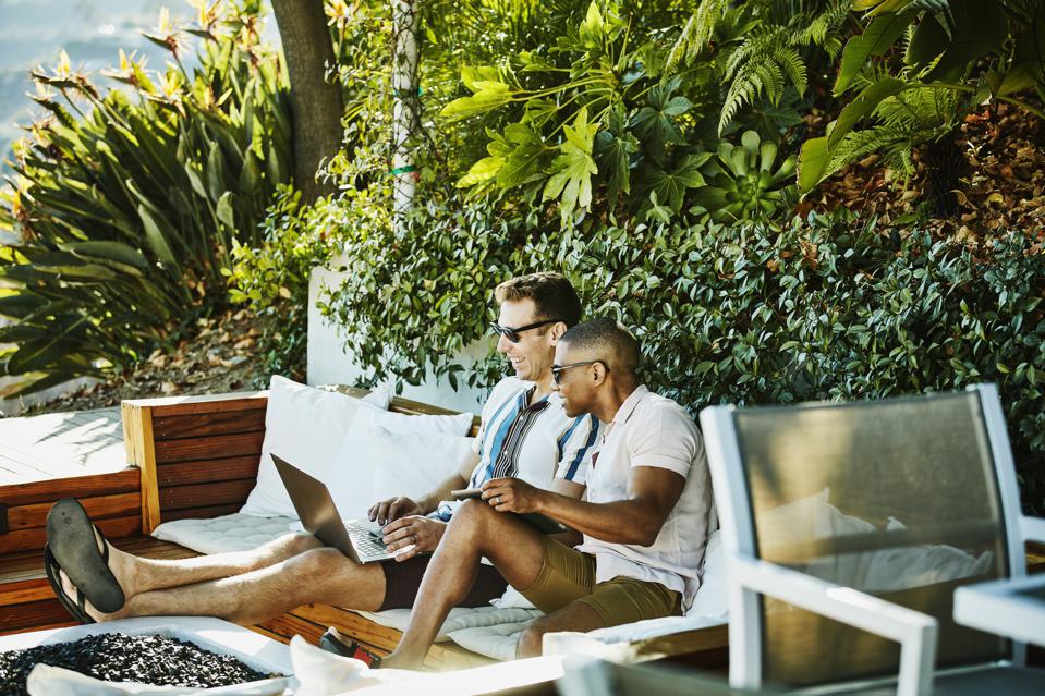 Smiling gay couple looking at laptop together in backyard