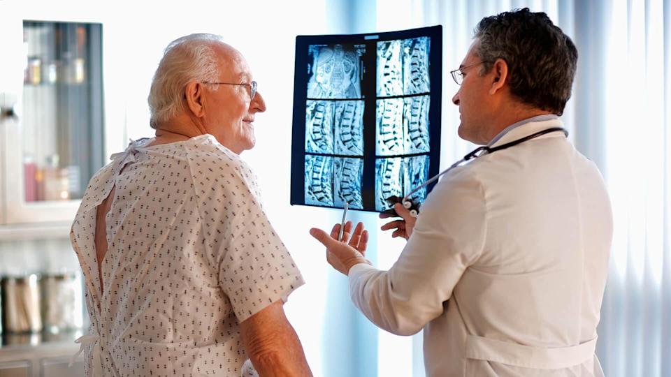 Doctor talking to senior male patient while holding up MRI.