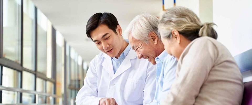 young doctor discussing test result and diagnosis with senior couple patients using digital tablet in hospital hallway